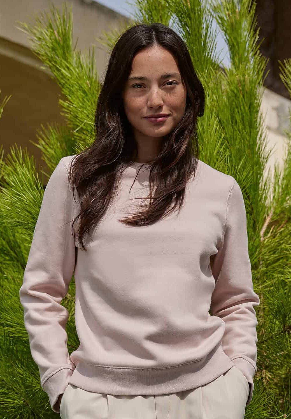 Elegant woman in casual sweatshirt standing outdoors with lush greenery, showcasing personalised embroidered workwear and uniform options from Dynamic Embroidery.