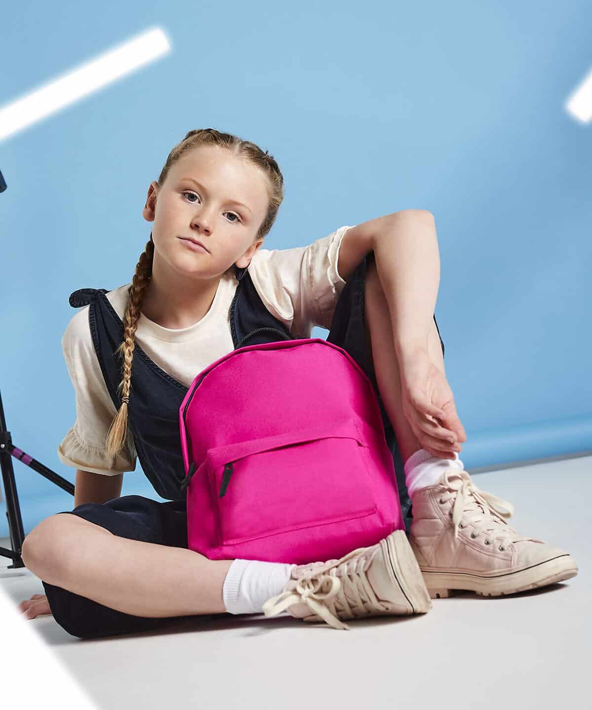Bright pink personalised embroidered school backpack resting on the floor with a young girl sitting next to it, showcasing customised workwear and school uniform embroidery.