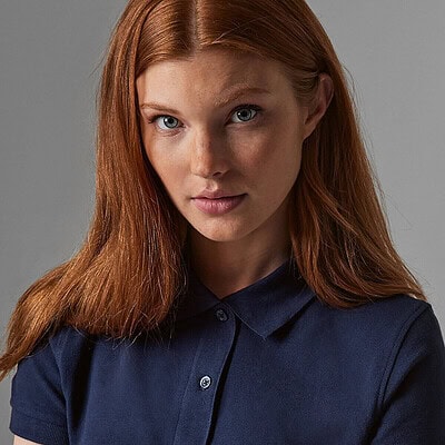 Woman wearing navy B&C Inspire Polo with embroidered logo.