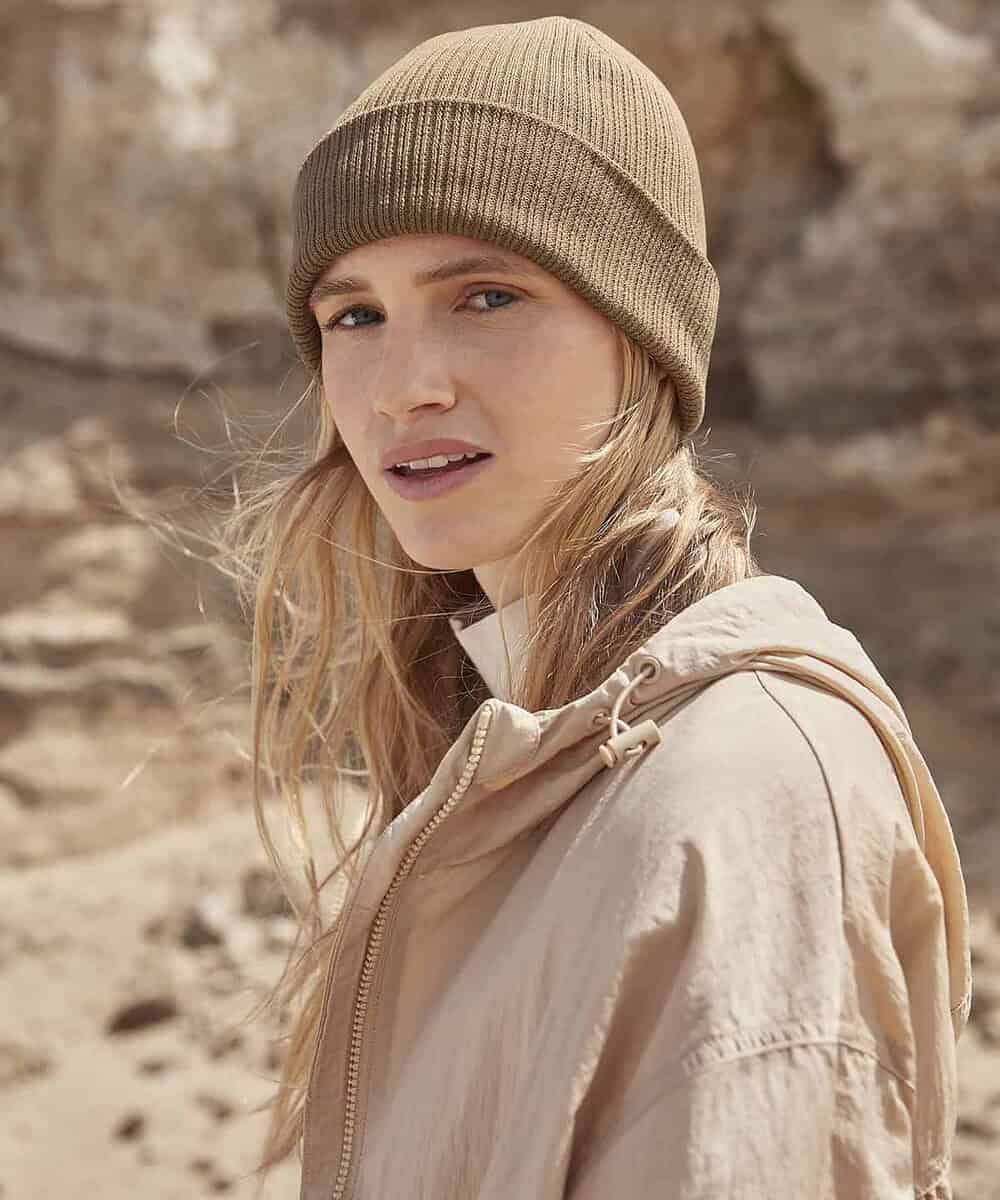 Woman wearing a beige ribbed beanie outdoors, showcasing the Beechfield B376R Polylana beanie.