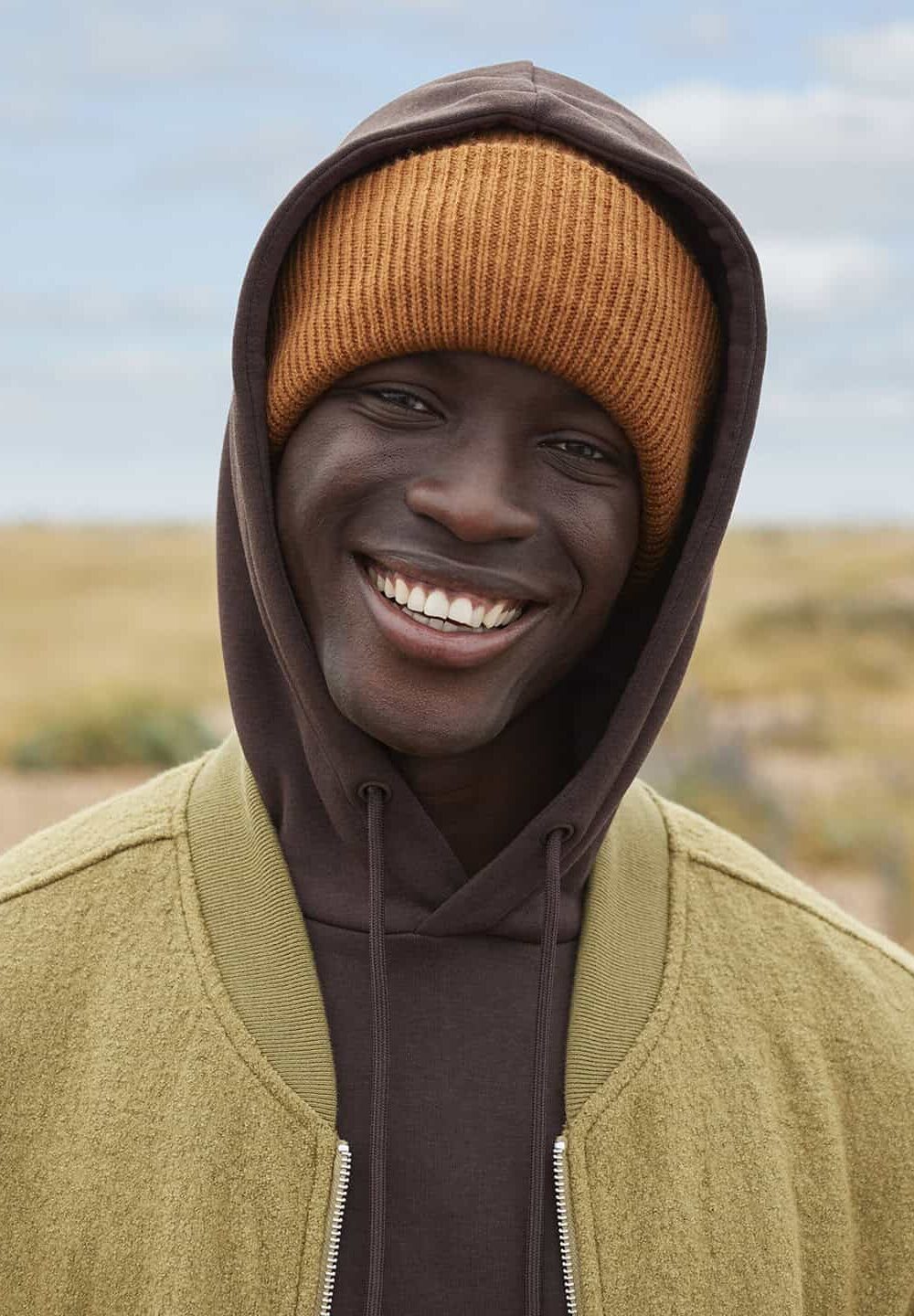 Bright smiling man in warm hooded sweatshirt and beanie, outdoor casual wear.