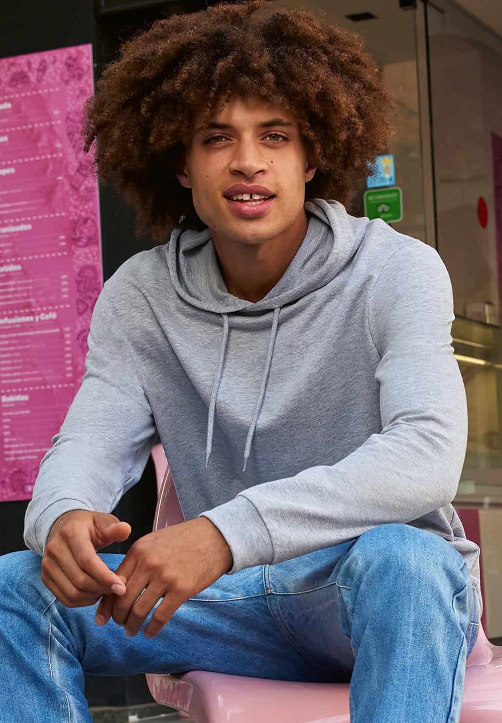 Bright young man wearing custom embroidered casual hoodie at shop entrance.