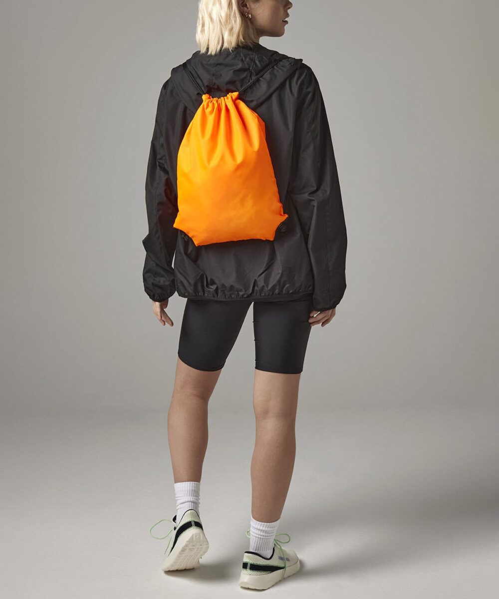 Bright orange Bagbase BG010 gymsac backpack on model's back.
