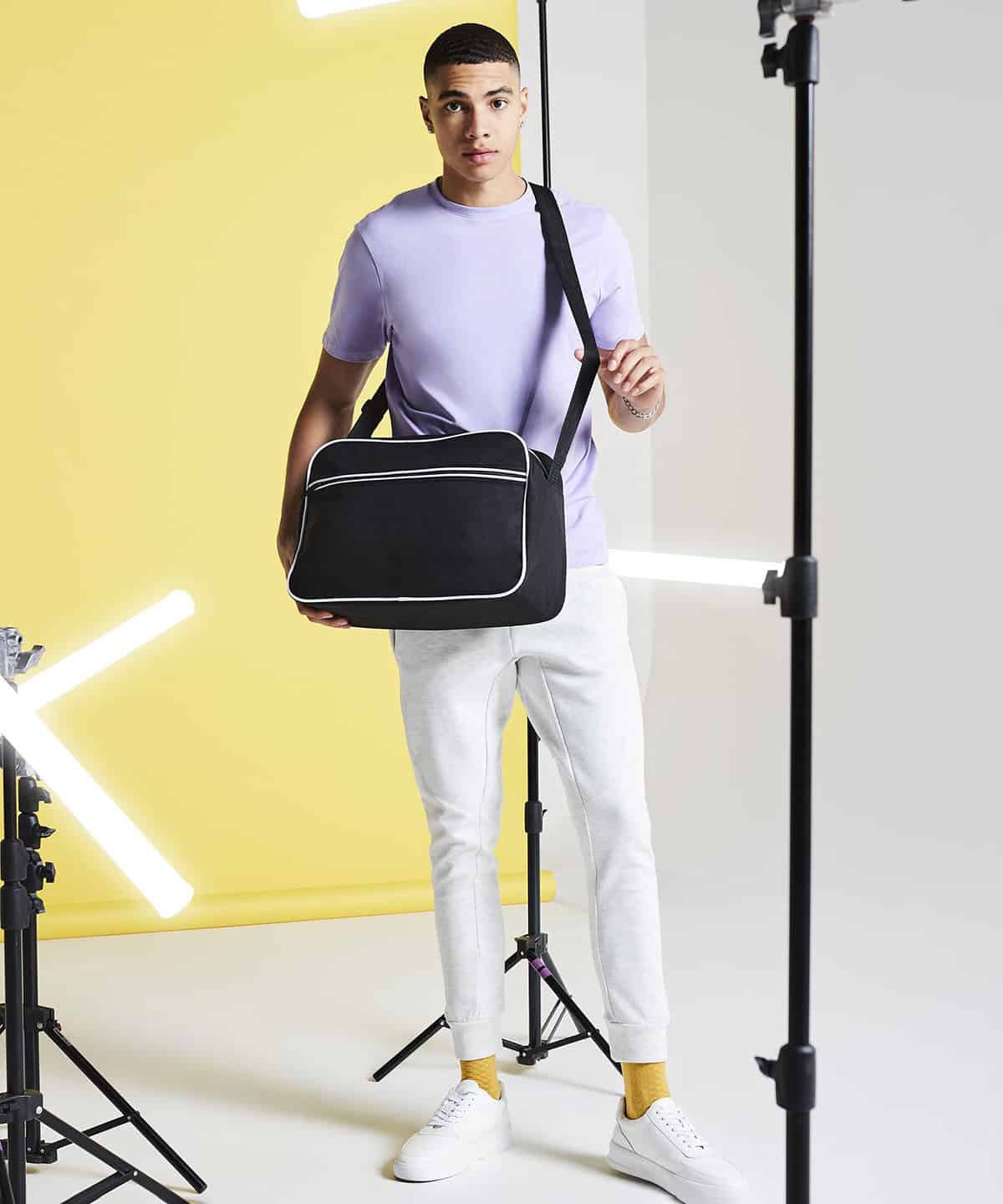 Youthful man in casual white attire holding a black shoulder bag, on professional photo shoot set.