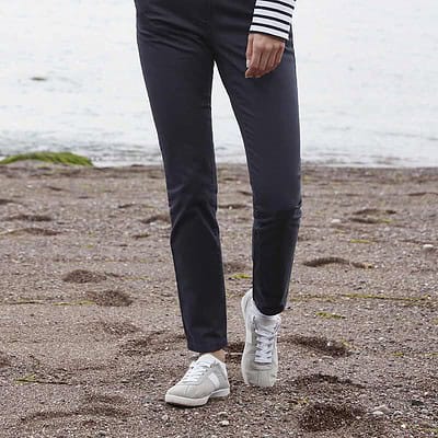 Woman wearing navy stretch chinos on a beach, suitable for work or casual settings.