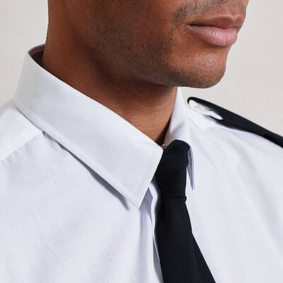Close-up of a person wearing a white shirt with black epaulettes and a black tie.