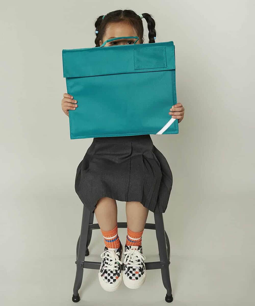 Child holding a personalised turquoise book bag for school.
