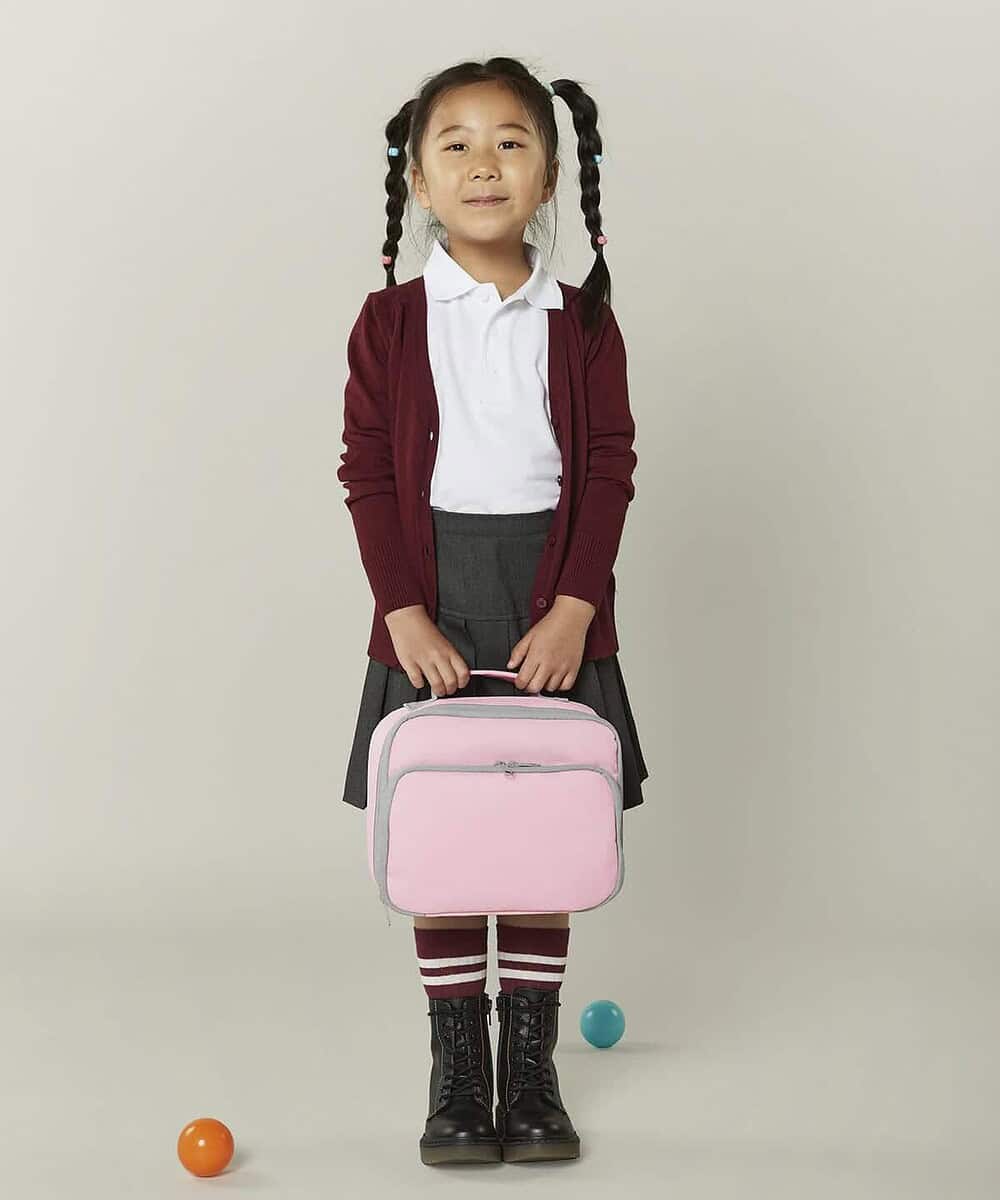 Schoolgirl with pink lunch cooler bag, standing against a plain background.
