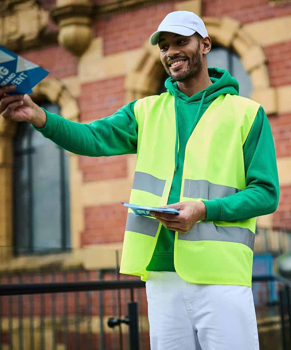 Man wearing high visibility vest and cap, smiling outdoors.