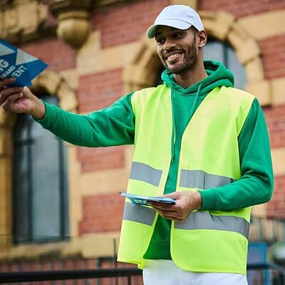 Man wearing high visibility vest and cap, smiling outdoors.