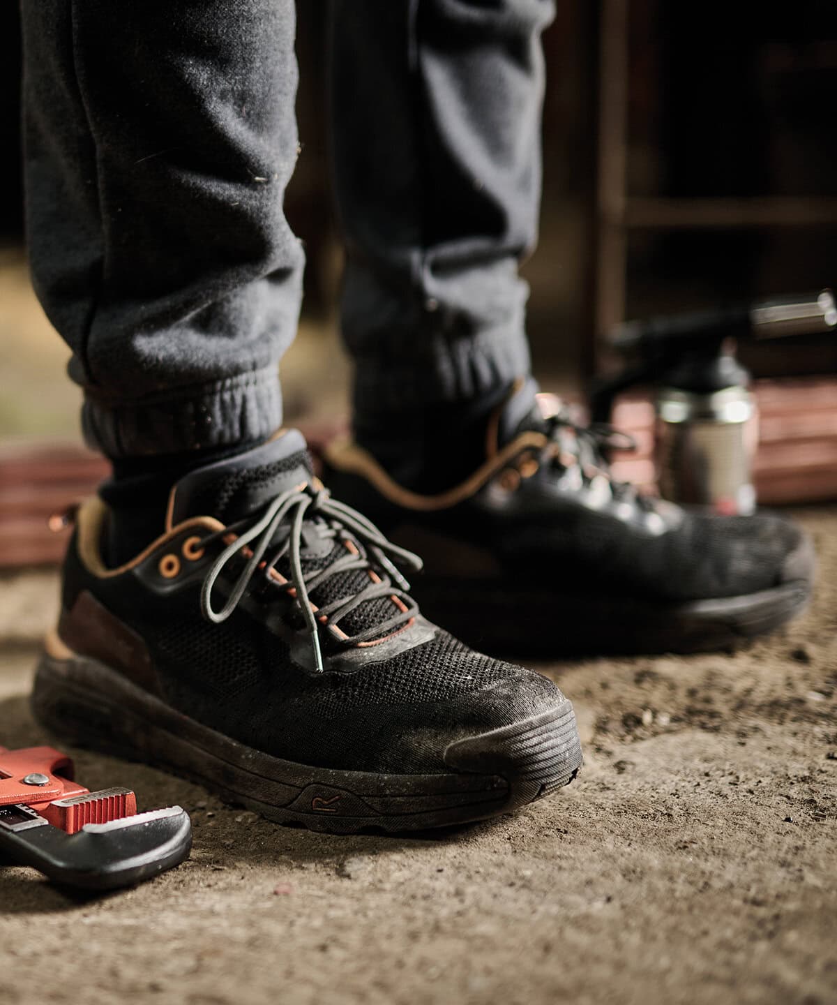 Comfortable black work boots with orange accents on a dusty floor.