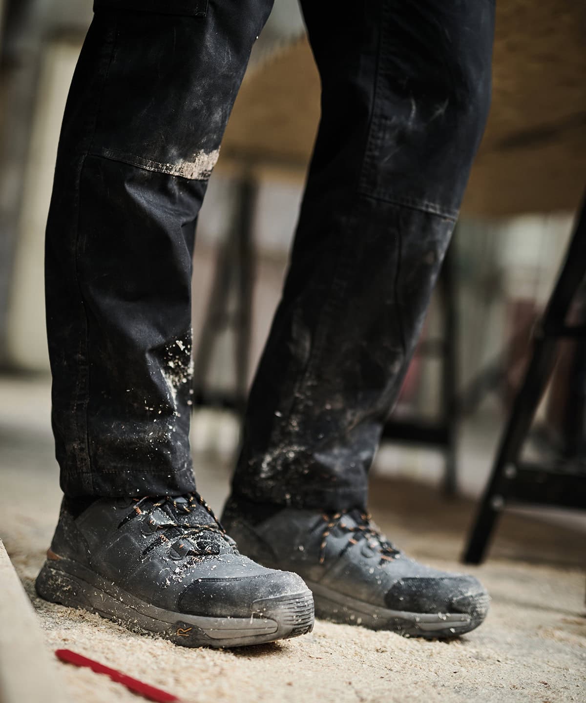 Black workwear trousers with paint splatters and durable safety shoes for construction or industrial work. Designed for embroidery of personalised uniforms for a professional appearance.