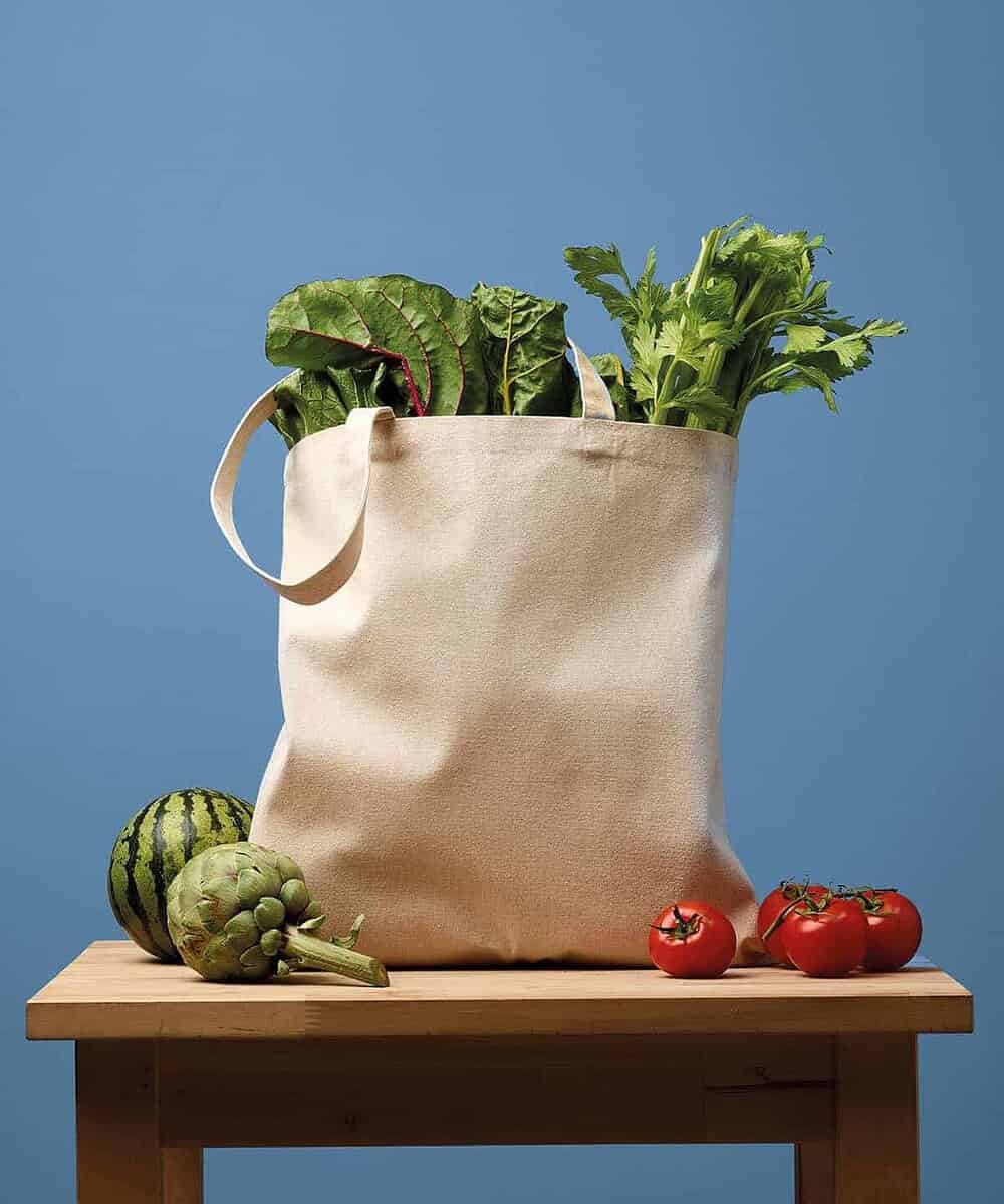 Recycled canvas shopping bag filled with fresh vegetables on a wooden table.