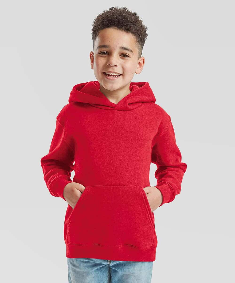 Child wearing a red Fruit Of The Loom SS873 kids hoodie, smiling and standing against a plain backgr.