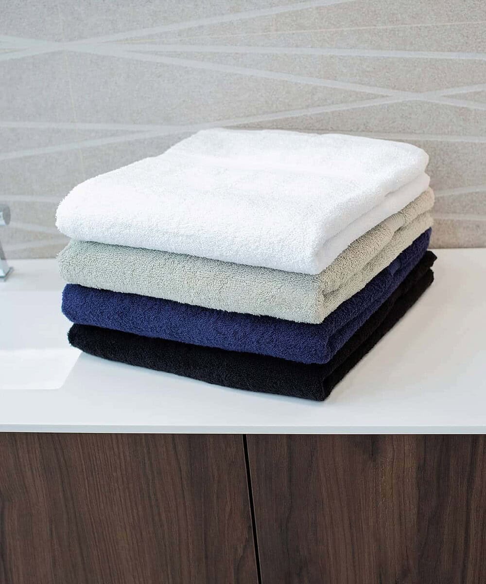 Stack of plush luxury bath towels in white, beige, navy, and black on a bathroom surface.
