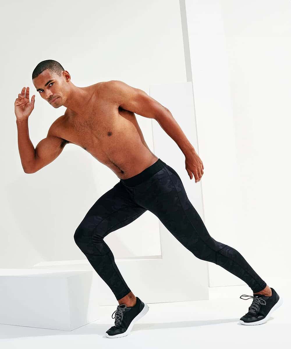Man in black Tridri® training leggings in a stretching pose.