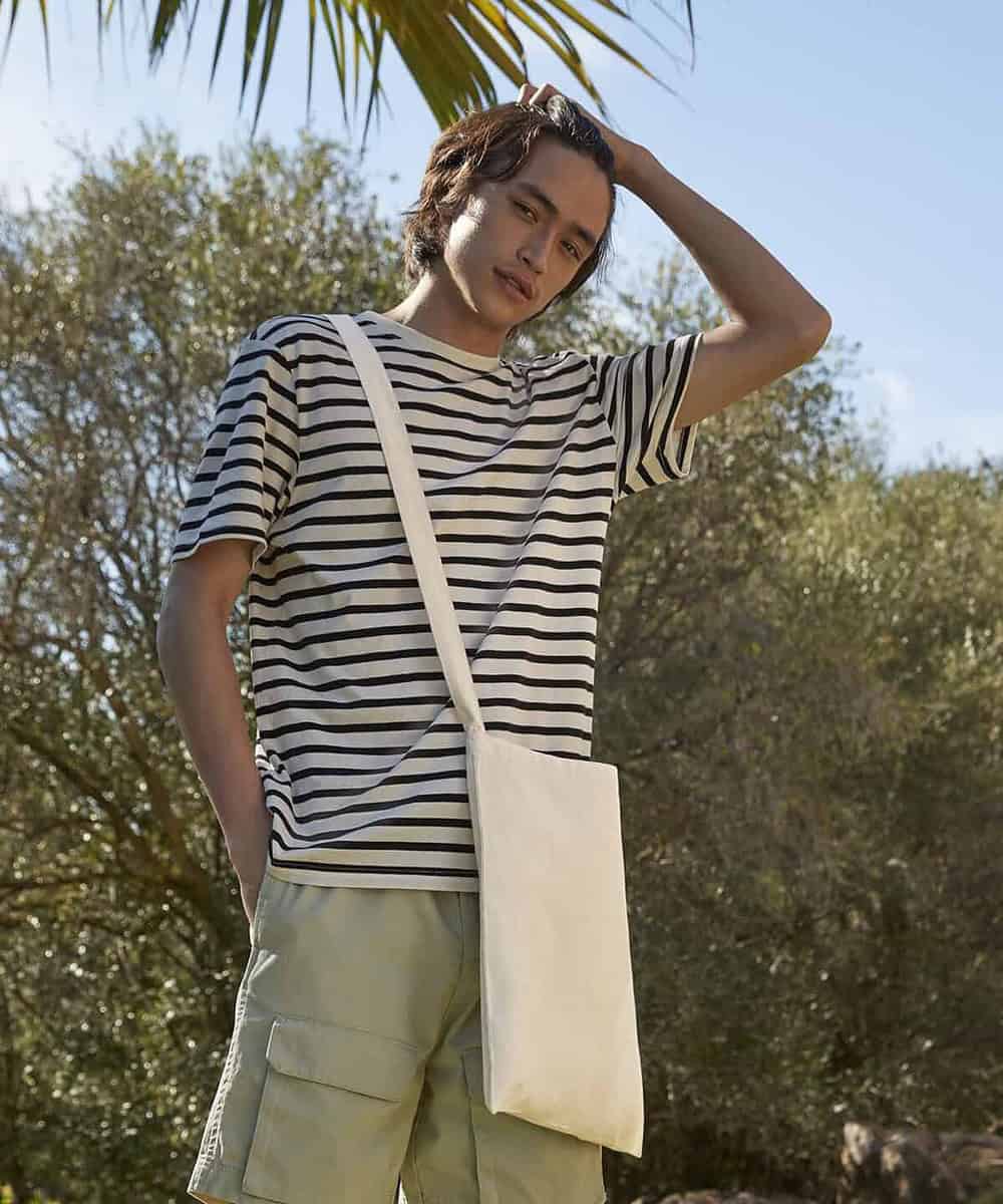 Woman wearing a striped t-shirt with a beige crossbody bag outdoors on a sunny day.