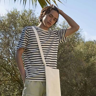 Woman wearing a striped t-shirt with a beige crossbody bag outdoors on a sunny day.