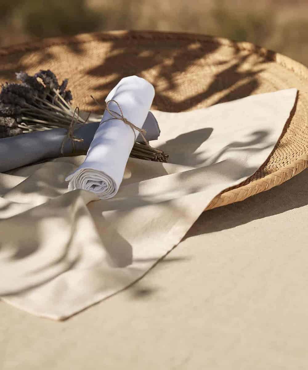 Embroidered white tea towel with logo, rolled and tied with twine, on a rustic surface.