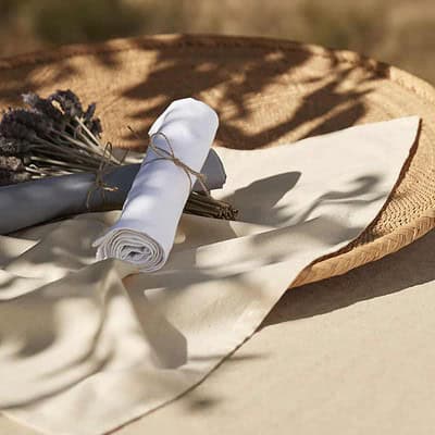 Embroidered white tea towel with logo, rolled and tied with twine, on a rustic surface.