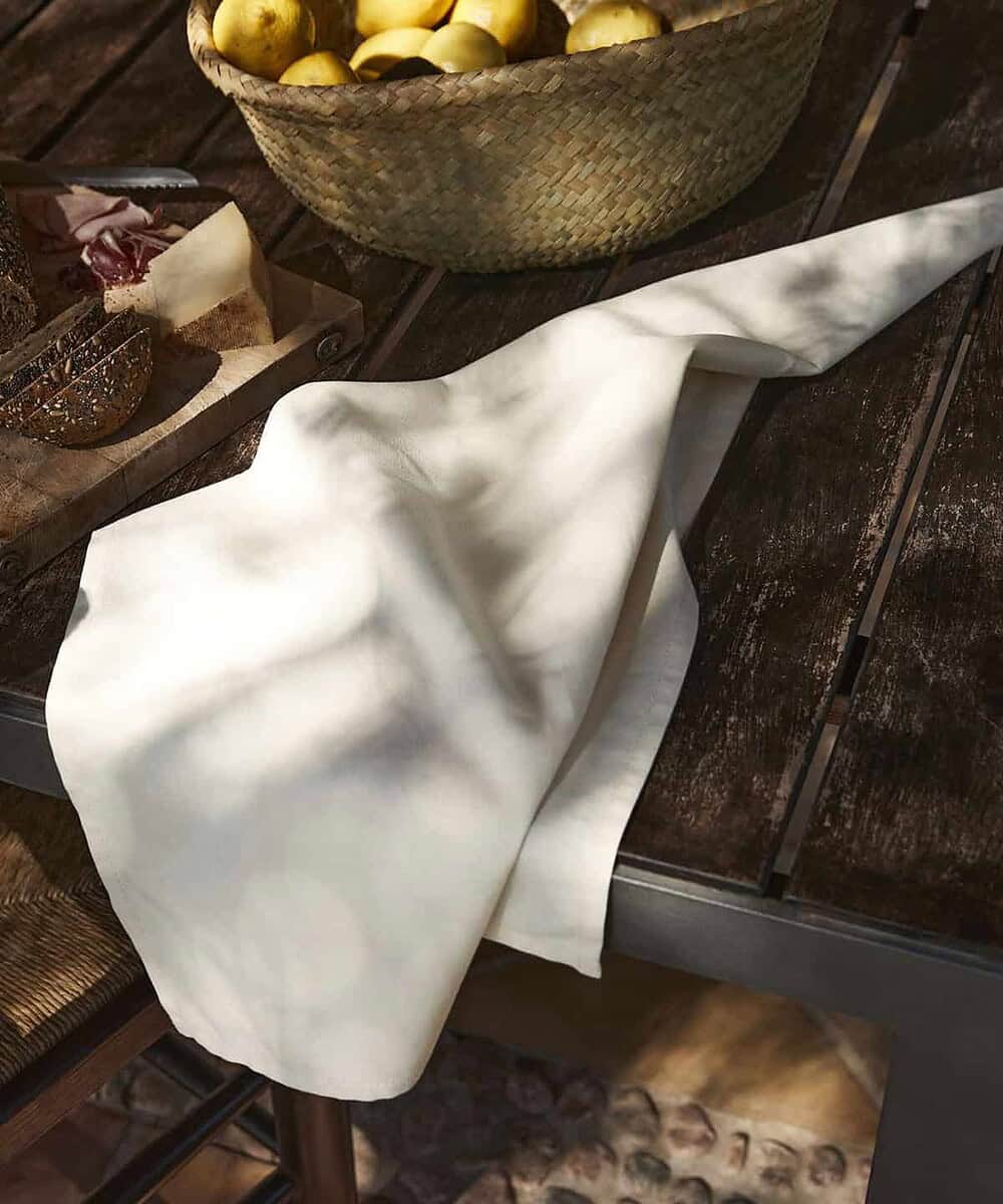 White organic cotton tea towel draped over a wooden table with baked goods and a basket of lemons.