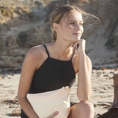 Woman holding a beige organic accessory bag on the beach, eco-conscious lifestyle.