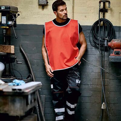 Man wearing Yoko YK009 Hi-Vis Reflective Border Tabard in workshop setting.